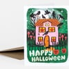 A folded greeting card featuring a Halloween illustration of a pink haunted house with jack-o'-lantern windows, black crows, bats, mushrooms, a cat, and the words "HAPPY HALLOWEEN" on the front.