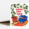 A folded greeting card with a botanical illustration of potted plant, blue pot, vegetables, mushrooms, and the red text "HERE FOR YOU" on the front.