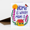 A folded greeting card with the text "HOME is where MOM is" and a colorful illustration of a yellow house, flowers, a sun, and a small bird.