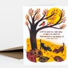 A folded greeting card shows an illustrated autumn tree with a yellow sun, a small bird on a branch, two dogs on the ground, fallen leaves, and the printed quote "I AM SO GLAD YOU ARE HERE. IT HELPS ME REALIZE HOW BEAUTIFUL MY WORLD IS. - RAINER MARIA RILKE".