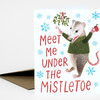A holiday greeting card shows a mouse in a green sweater holding a candy cane and a red mug beside the text "Meet Me Under The Mistletoe" with blue snowflakes and a sprig of mistletoe.