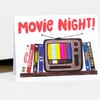 A greeting card with the text "Movie Night!" above an illustration of a retro television showing color bars, flanked by a row of VHS tapes or movie cases.