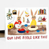 A greeting card featuring a watercolor illustration of two rabbits in a kitchen scene with hanging plants, shelves, cups, fruit, and the text "OUR LOVE FEELS LIKE THIS".