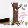 A folded greeting card with an illustrated tree, two squirrels, small red hearts, and the text "HAPPY VALENTINE'S DAY" on the front.