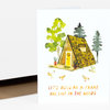 A folded greeting card shows an illustrated A-frame house in the woods with trees, three chickens, and the text "LET'S BUILD AN A-FRAME AND LIVE IN THE WOODS" on the front.