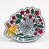 A die-cut enamel pin shaped like a flower with a spider web in the center, red blossoms, green leaves, and the text "IT'S ALL CONNECTED" along the bottom edge.