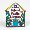 A house-shaped enamel pin with the words "Defend Public Libraries," decorated with a blue door, flowers, leaves, and a yellow roof.