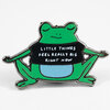 An enamel pin shaped like a green frog wearing a black shirt that reads "LITTLE THINGS FEEL REALLY BIG RIGHT NOW" with a blue belly and silver outline.