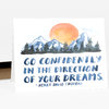 A folded greeting card with a watercolor mountain and pine tree illustration, a large orange sun, and the printed quote “GO CONFIDENTLY IN THE DIRECTION OF YOUR DREAMS. -HENRY DAVID THOREAU.”