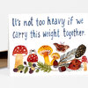 A greeting card with the hand-lettered text "It's not too heavy if we carry this weight together." above watercolor mushrooms, leaves, berries, a moth, and acorns.