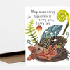 A folded greeting card with the text "May moments of exquisiteness carry you, carry us." and a watercolor woodland illustration featuring leaves, mushrooms, ferns, a spiral frond, and small insects.