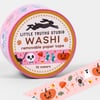 A roll of pink washi tape labeled "LITTLE TRUTHS STUDIO WASHI removable paper tape 10 meters" with Halloween-themed icons including a bat, skull, pumpkin, spider, mushroom, candy, and socks on the visible tape.