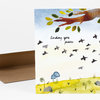 A folded greeting card with the handwritten-style text "Sending you peace" and an illustration of birds, leaves, a tree branch, and a grassy scene.