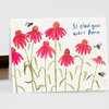 A folded greeting card with hand-painted pink flowers and bees, with the text "So glad you were born" on the front.