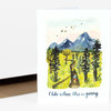 A folded greeting card with a watercolor illustration of two people on a winding trail through trees toward blue mountains and the handwritten text "I like where this is going."