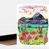 A folded greeting card shows a watercolor landscape with dark mountains, flying birds, wildflowers, and a butterfly, with the handwritten text “wildflowers on your birthday.”