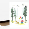A folded greeting card with a watercolor woodland scene showing tall evergreen trees, birds, balloons, wrapped gifts, and a party hat.