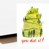 A folded greeting card with an illustrated green terraced hill, trees, and a cyclist, with the words "you did it!" printed in orange script on the front.