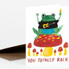A folded greeting card featuring a green frog holding up a guitar and a flame while sitting on a red mushroom, with the text "YOU TOTALLY ROCK" printed at the bottom.