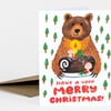 A folded greeting card shows a bear holding a decorated log with mushrooms and holly, with the text "HAVE A VERY MERRY CHRISTMAS!" in red.