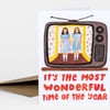 A greeting card with an illustrated vintage television showing two girls in blue dresses, and the text "IT'S THE MOST WONDERFUL TIME OF THE YEAR" in large red letters.