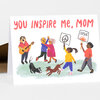 A folded greeting card with the text "YOU INSPIRE ME, MOM" and an illustration of several people with dogs, including two people holding protest signs.