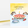 A folded greeting card with a watercolor-style illustration of two cats peeking over a table, a strawberry pie with a lit candle, and the text "HAPPY BIRTHDAY, SWEETIE PIE."