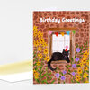 A folded birthday greeting card with the text "Birthday Greetings," featuring a black cat wearing a party hat in a window surrounded by flowers and colorful bunting.