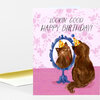 A folded birthday card shows a brown cat wearing a party hat and looking into a blue standing mirror, with the text “LOOKIN’ GOOD HAPPY BIRTHDAY!” on a pink floral background.