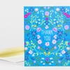 A blue folded thank-you card with a colorful floral pattern and the words "THANK YOU" in white on the front.