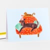 A folded greeting card with an illustration of a dark brown dog wearing a striped party hat, sleeping on an orange floral couch with a small cat lying on top.