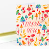 A folded thank you notecard with a colorful mushroom and leaf pattern and the words "thank you" in red script on the front.