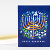 A vertical greeting card with a blue front featuring a menorah made of leafy branches, eight lit candles, birds, flowers, and the text "HAPPY HANUKKAH" at the bottom.