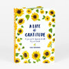 A hardcover journal with a white cover bordered by yellow sunflowers and green leaves, titled "A LIFE of GRATITUDE" and "A Journal to Appreciate It All, Big and Small," with "LORI ROBERTS" on the front and spine.