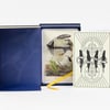 A boxed illustrated card deck with a blue case, a ribbon pull, and a cream cover card reading "100 Divinations for Uncertain Days" and "Maria Popova."