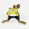 A small enamel pin shaped like a bright yellow frog doing a squat with a gold outline and dark blue lower half.