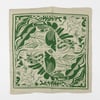 A square cream bandana with a green border and an allover abstract dinosaur-and-leaf print.
