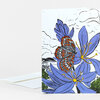 A folded greeting card with a colorful illustration of a butterfly on purple-blue camas flowers, with an envelope partially visible behind it.