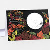 A folded greeting card with a black cover decorated with colorful autumn leaves around a large white full moon shape.