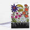 A folded greeting card features a colorful illustrated garden of flowers with visible roots and no readable text on the front.
