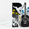 A folded greeting card with a black-and-white illustration of a guitar, a flying dove, flowers, and a key, accented with yellow and blue flowers.