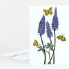 A folded greeting card with a botanical illustration of three tall blue lupine flowers and four yellow butterflies on a white front.