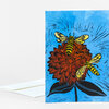 A folded greeting card shows a blue floral illustration with a large red zinnia and two yellow-and-black bees, with a plain white envelope partially visible behind it.