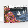 A folded greeting card with a colorful illustrated scene of pink bay blossoms in the foreground, blue water with two sailboats, and dark mountains with birds in the distance.