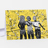 A folded greeting card with a bright yellow cover featuring three black-and-white illustrated figures seen from behind among black flowering branches, with no visible text.