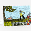 A folded greeting card with a colorful illustrated scene of a person gardening with a rake or hoe among flowers, trees, and a basket.