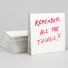 A stack of square white paper pads, with the front pad printed in red handwritten-style text reading "REMEMBER ALL THE THINGS!!"