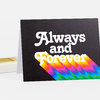 A folded black greeting card with large white text reading "Always and Forever" and a diagonal rainbow graphic across the lower half.