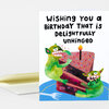 A folded birthday greeting card with the text "Wishing You a Birthday that is Delightfully Unhinged" and an illustration of two green monster characters hugging a slice of cake with a lit candle.