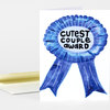 A folded greeting card with a large blue award ribbon graphic and the text "CUTEST COUPLE AWARD" in black on the front.
